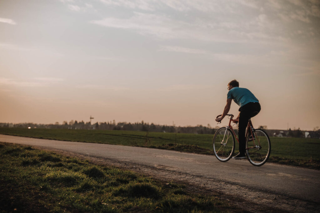 Junger Mann fährt auf einem Feldweg bei Sonnenuntergang mit dem Fahrrad