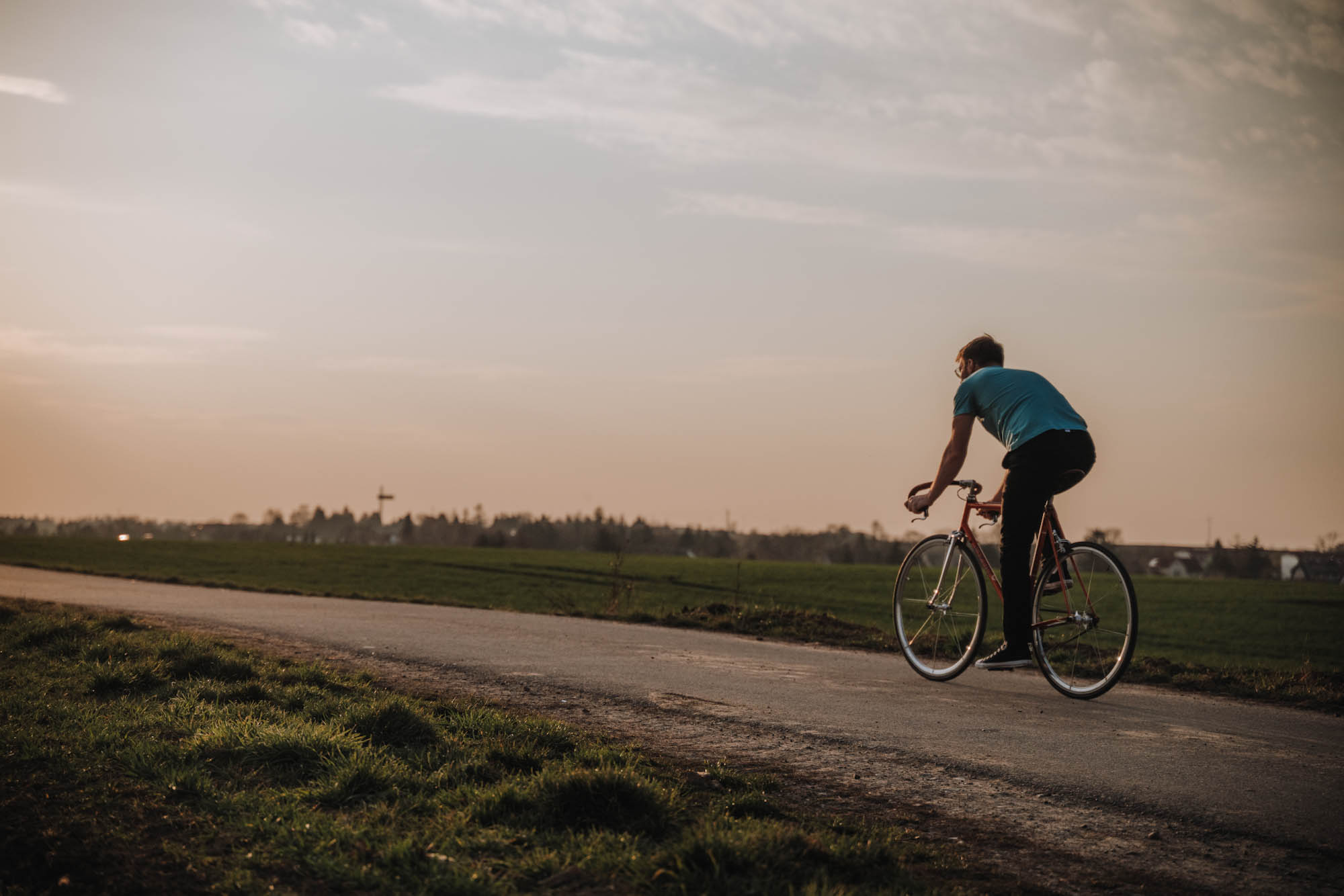 Junger Mann fährt auf einem Feldweg bei Sonnenuntergang mit dem Fahrrad